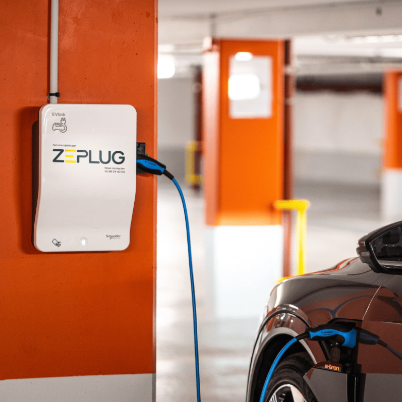 Photo d'une borne de recharge Zeplug dans un parking sous-terrain, reliée à un véhicule en recharge.