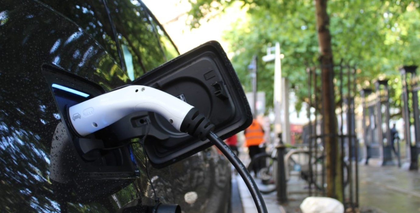 Cordon de recharge branché sur une voiture électrique stationnée sur une place