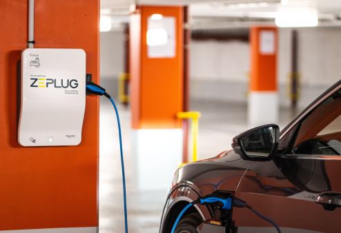 Voiture se rechargeant à une borne de recharge blanche murale Zeplug dans un parking