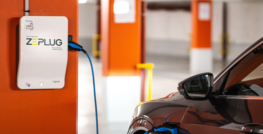 Voiture se rechargeant à une borne de recharge blanche murale Zeplug dans un parking