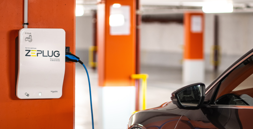 Voiture se rechargeant à une borne de recharge blanche murale Zeplug dans un parking