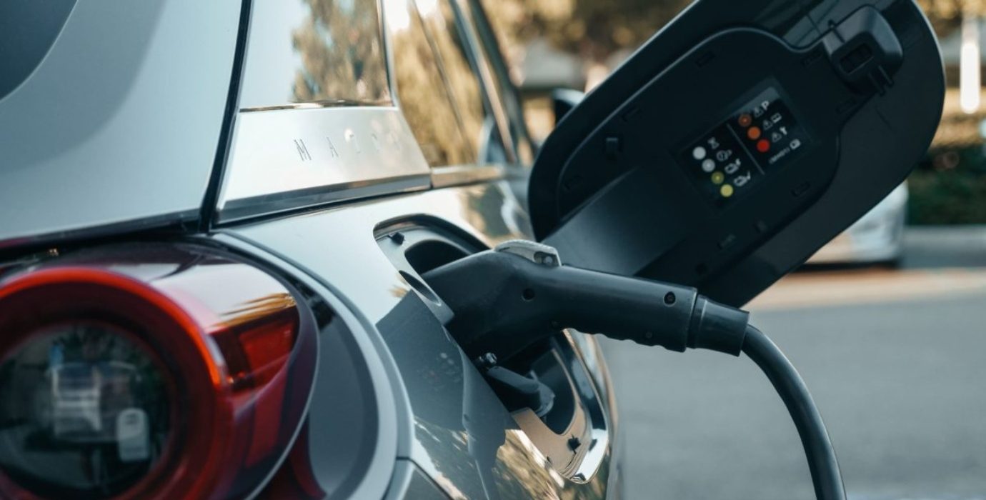 Voiture électrique branchée par un cordon de recharge dans un parking extérieur