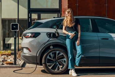 Femme adossée à son véhicule électrique en cours de charge