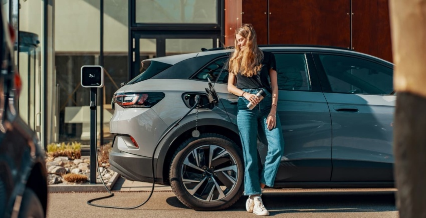 Femme adossée à son véhicule électrique en cours de charge
