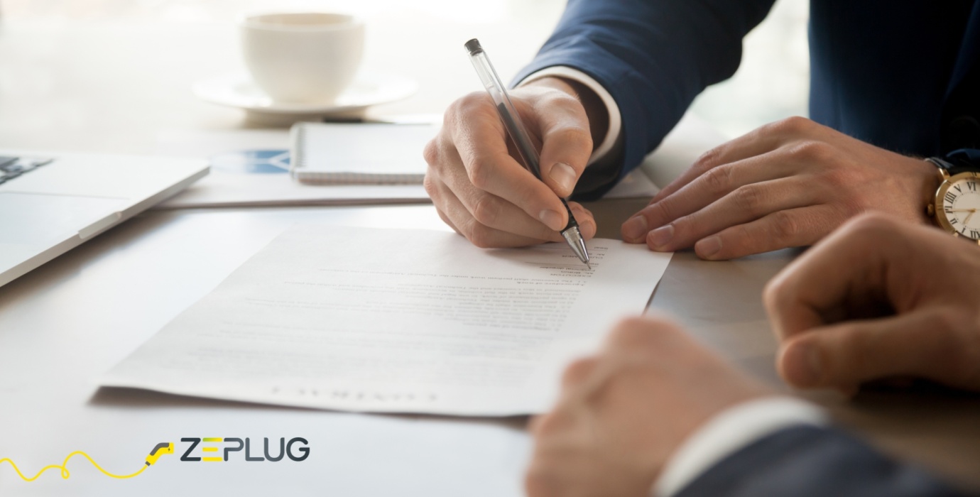 Signature d’un contrat par un professionnel en costume dans un environnement de bureau, avec un ordinateur portable et une tasse de café sur la table.