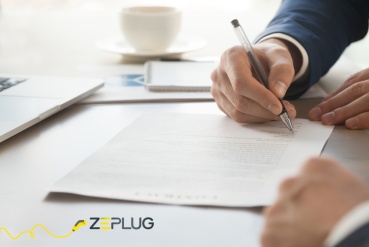 Signature d’un contrat par un professionnel en costume dans un environnement de bureau, avec un ordinateur portable et une tasse de café sur la table.