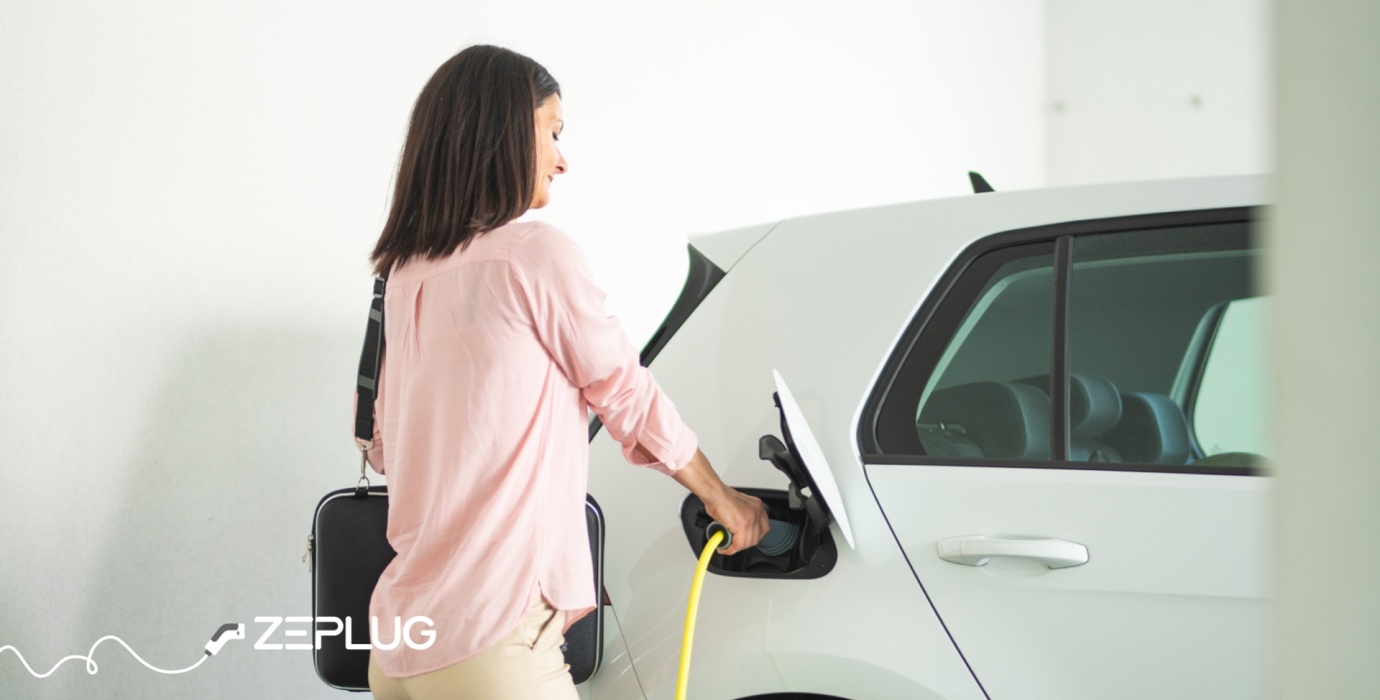 Femme branchant son câble de recharge à sa voiture électrique, tenant un sac de travail, dans un cadre lumineux et moderne.