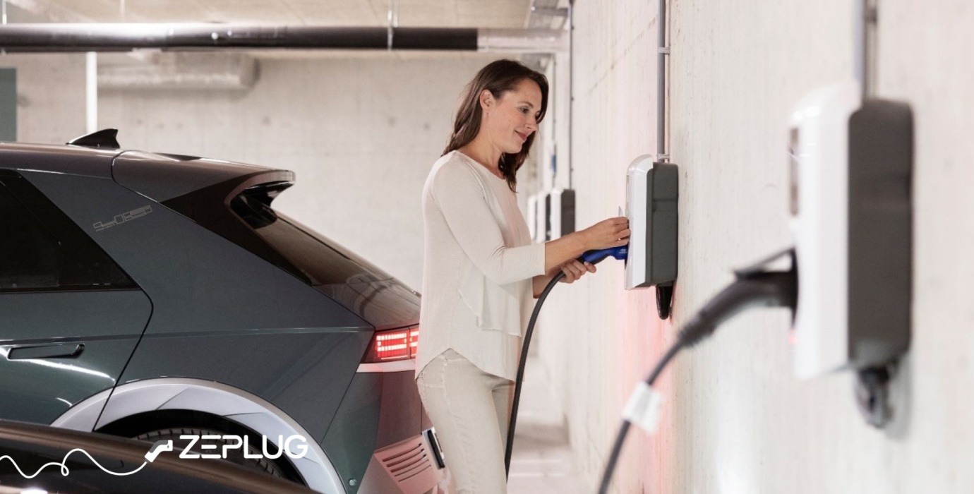 Femme branchant son câble de recharge, à une borne de recharge, dans un parking lumineux.