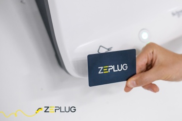 Photo en gros plan d'un badge Zeplug, devant une borne de recharge.