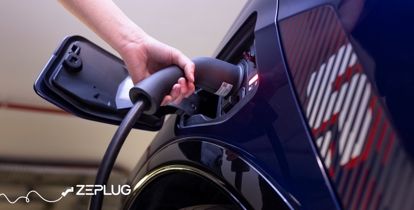 Main qui branche un câble de recharge dans la prise de recharge d'une voiture électrique.