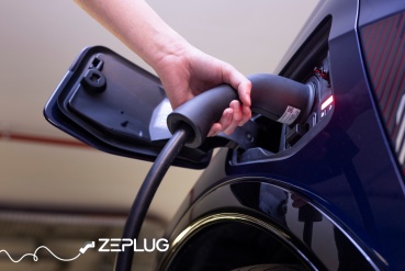 Main qui branche un câble de recharge dans la prise de recharge d'une voiture électrique.