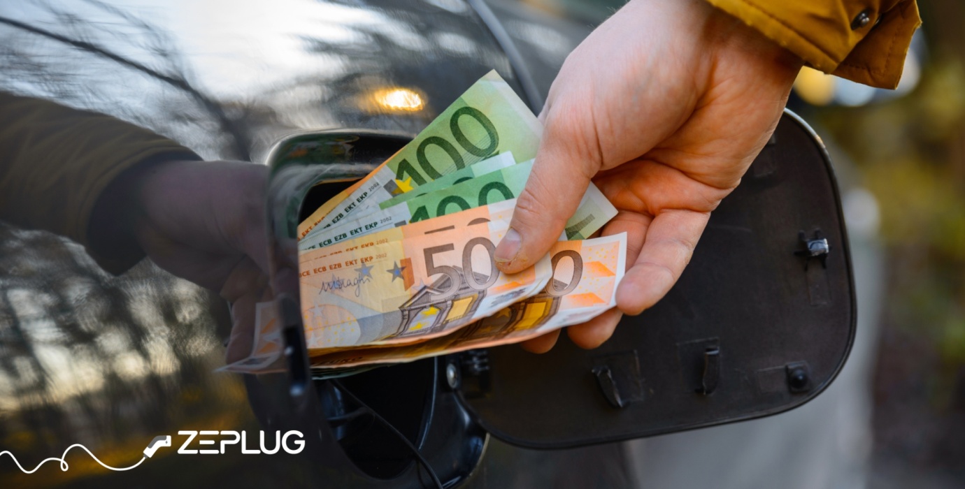 Main qui met des billets de cents et de cinquante dans la prise de recharge d'une voiture électrique.
