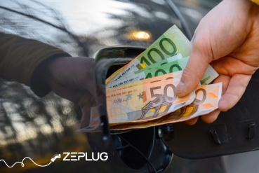 Main qui met des billets de cents et de cinquante dans la prise de recharge d'une voiture électrique.